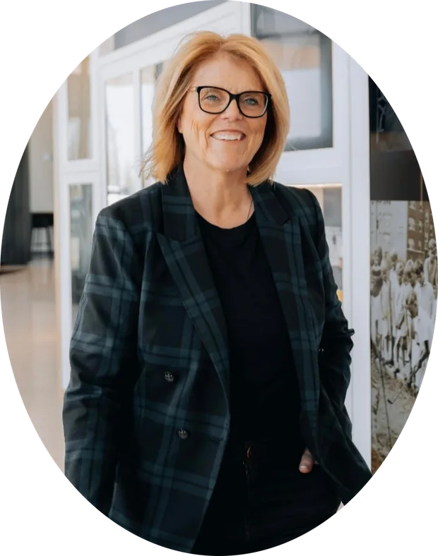 Ann Sowieja smiling, in a plaid blazer and glasses