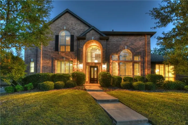 Brick two-story home at dusk with warm lights in the windows